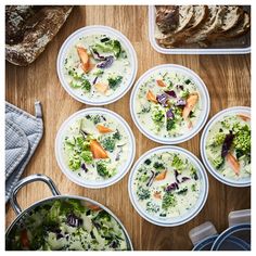 four bowls of broccoli and carrots with bread in the background on a wooden table