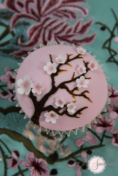 a cupcake decorated with pink and white flowers on a blue tablecloth next to a tree