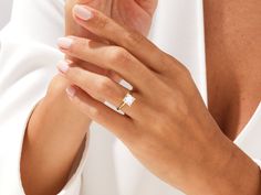 a woman's hand wearing a gold ring with a square shaped diamond on it