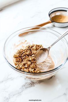 a glass bowl filled with oatmeal next to two spoons on a white counter