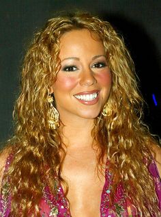 a woman with long curly hair smiling at the camera while wearing gold earrings and a purple dress