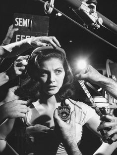 black and white photograph of woman getting her hair combed by several people in the background