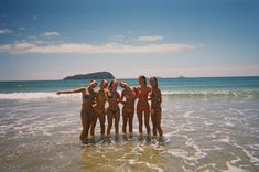 four women standing in the ocean with their arms around each other and pointing at something