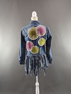 a blue jean jacket with pink, yellow and green flowers on the back that has fringes