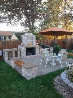 an outdoor patio with table, chairs and fire place in the middle of it is surrounded by green grass