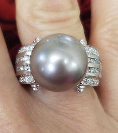 a woman's hand holding a ring with a gray pearl and diamonds on it