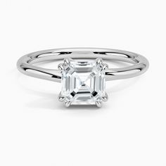 an emerald cut diamond ring on a white background with the center stone in the middle