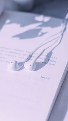 two white earbuds laying on top of an open book with the shadow of a person's head