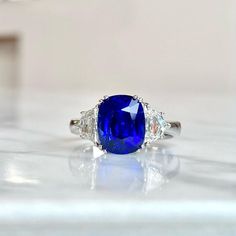 a blue and white diamond ring with three diamonds on the side, sitting on a table