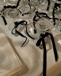 several wine glasses with black bows are on a white table cloth, ready to be used as centerpieces