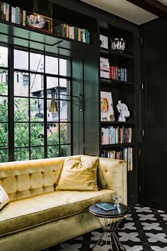 a yellow couch sitting in front of a book shelf filled with lots of books next to a window