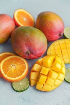 mangoes, oranges and limes cut in half on a counter top with one sliced up