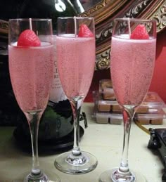 two champagne flutes filled with pink liquid and topped with raspberries are sitting on a table