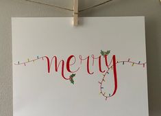 a christmas card hanging on a clothes line with the word merry written in red and green