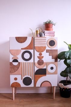 a white cabinet with geometric shapes painted on the front and sides, next to a potted plant