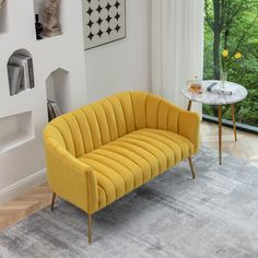 a yellow couch sitting in front of a window next to a table with a vase on it