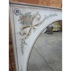 an ornate wooden mirror frame with flowers and leaves painted on the side, sitting in a warehouse