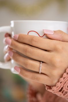 a woman's hand holding a coffee cup with a diamond ring on top of it