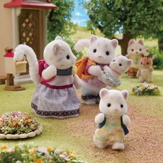 three white kittens are standing in front of a small house and some flowers on the ground