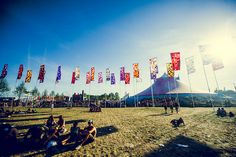 people are sitting on the ground in front of tents with flags flying from them at an outdoor event