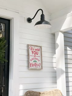 a christmas sign hanging on the side of a white house next to a wicker basket