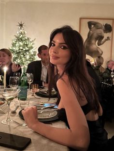 a woman sitting at a table in front of a christmas tree with wine glasses on it