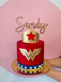 a cake with the name sandy written on it and a wonder woman hat topper