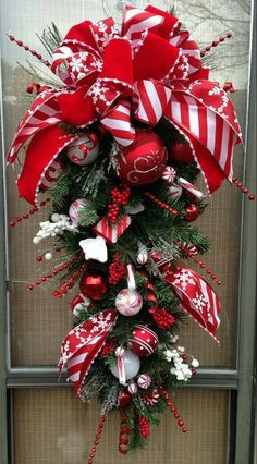 a red and white christmas wreath with candy canes, ornaments and bows on the front door