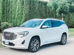 a white gmc suv parked on the side of the road in front of some bushes