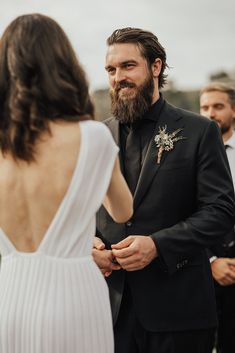 a man with a beard wearing a suit and standing next to a woman in a white dress