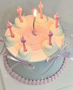 a birthday cake with lit candles and pink ribbon around it's edges on a white table