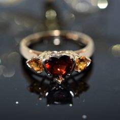 A Ladies 14K Yellow Gold Ring Set With A 6X6 Mm Heart Cut Red Garnet And 2 - 4X4 Mm Heart Cut Orange Garnets. The Ring Is Size 9 Heirloom Heart-shaped Gemstone Ring, Red Heart-shaped Rings With Center Stone, Heirloom Birthstone Rings For Valentine's Day, Red Heart Ring For Anniversary In Fine Jewelry Style, Fine Jewelry Red Heart Ring For Anniversary, Red Heart Ring For Anniversary, Fine Jewelry, Red Heart Shaped Rings With Accent Stones, Red Heart-shaped Rings With Accent Stones, Red Heart Shaped Fine Jewelry Rings