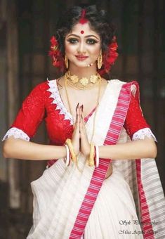 a woman in a red and white sari holding her hands together with both hands