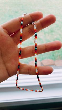 a hand holding a beaded necklace in front of a window