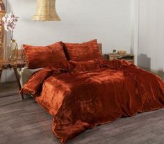 a bed covered in an orange comforter and pillow case next to a wooden table