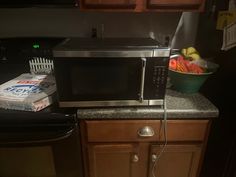 a microwave oven sitting on top of a kitchen counter next to a bowl of fruit