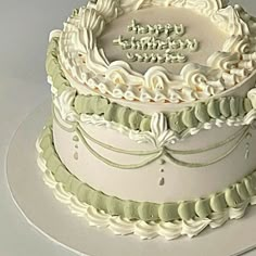 a three tiered cake with white frosting and green trimmings on a plate