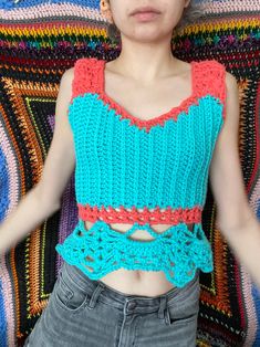 a woman wearing a crochet top and jeans standing in front of a colorful blanket