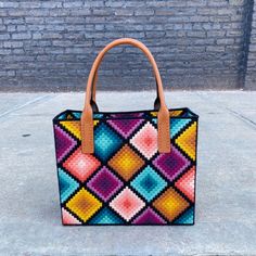 a colorful handbag sitting on top of a cement floor next to a brick wall