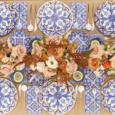 an overhead view of a blue and white table setting with plates, silverware and flowers