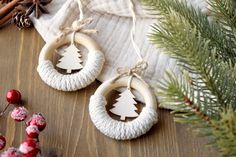 two wooden christmas ornaments hanging from strings next to pine cones and cinnamon sticks on a table