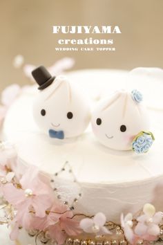 two small white cake topped with frosting and decorations on top of a table next to pink flowers