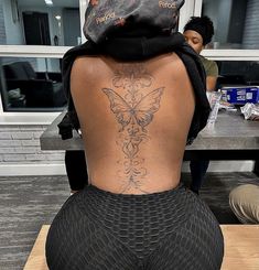 a woman with a butterfly tattoo on her back sitting in front of a counter top