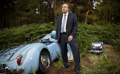 a man in a suit standing next to a blue car