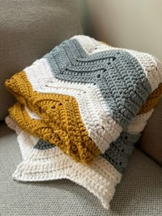 a crocheted blanket sitting on top of a gray couch next to a pillow