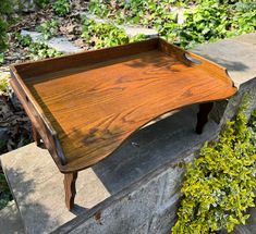 a wooden tray sitting on top of a stone wall next to green plants and bushes