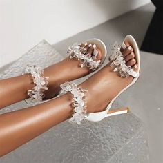 woman's feet wearing white high heels with flowers on the toe and ankle straps