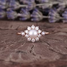 a pearl and diamond ring sitting on top of a piece of wood with lavenders in the background