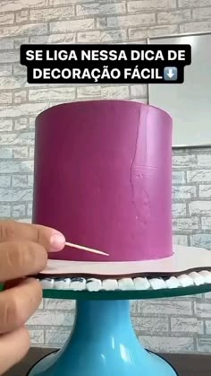 a person is decorating a purple cake with white icing on a blue pedestal