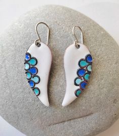 These earrings have the design of bird wings. Minimalist in style but they have a meticulous work. Earrings with a white background and blue scales, made by hand in enameled copper applying the cloissoné technique, which consists of the integration of metallic threads in the enamel, to create divisions in which enamel is applied. They can also be made in other colors. Light and comfortable to wear earrings. Enameling Jewelry, Terracotta Jewellery Making, Cloisonne Enamel Jewelry, Copper Jewellery, Terracotta Jewellery, Bird Wings, Enameled Copper, Jewelry White, Wings Design